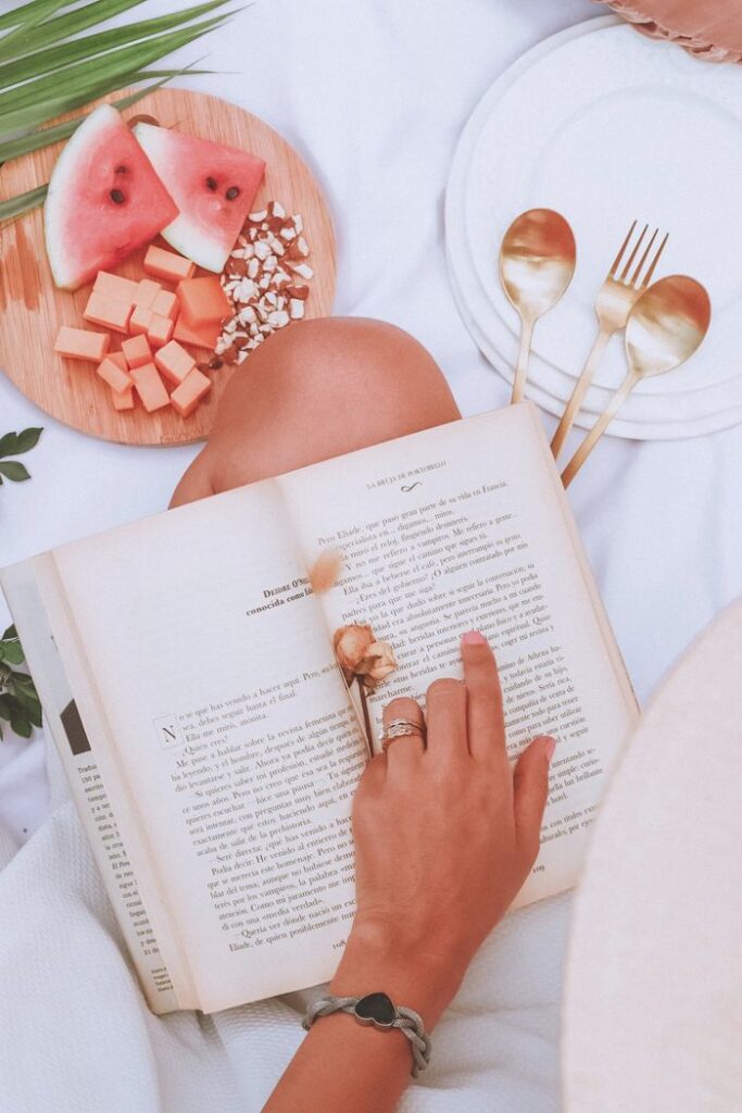 Relaxing outdoors with a book and fresh fruit platter on a sunny day, perfect for leisure.