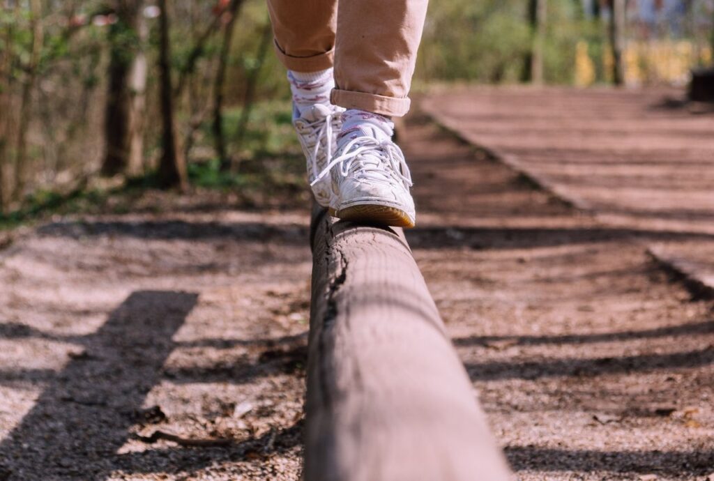 Close-up of a person walking on a wooden beam in a park setting, showcasing balance and focus.